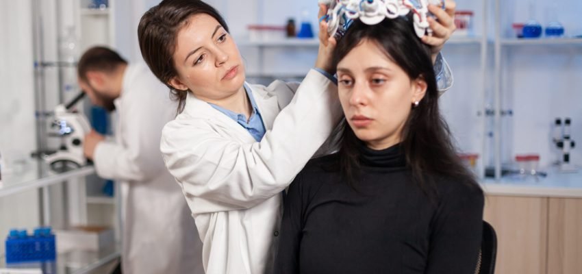 Neurologist in moden clinic preparing patient headset with sensors for brain scan with high tech technology device, tomography. Searching diagnosis for ill nervous system.